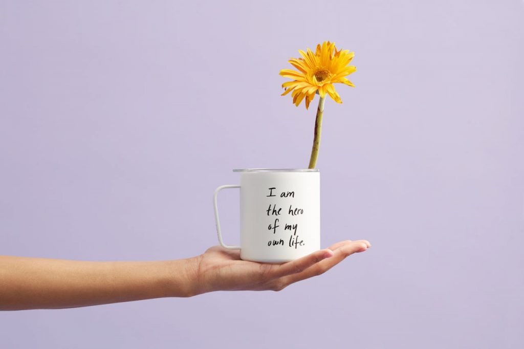 pexels photo 2228585 Hand holding a mug with a sunflower and motivational quote, set against a purple background.